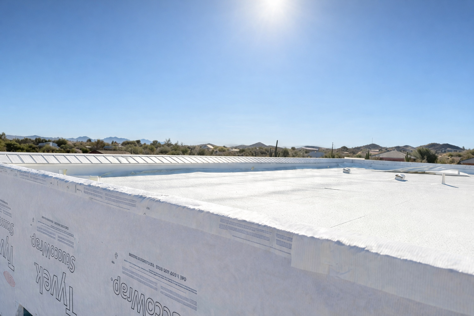 Roof installation featuring white TPO roofing with Tyvek Stuccowrap wall covering, set against a desert landscape with mountains and homes. Ideal for Arizona roofing, Glendale, Phoenix.