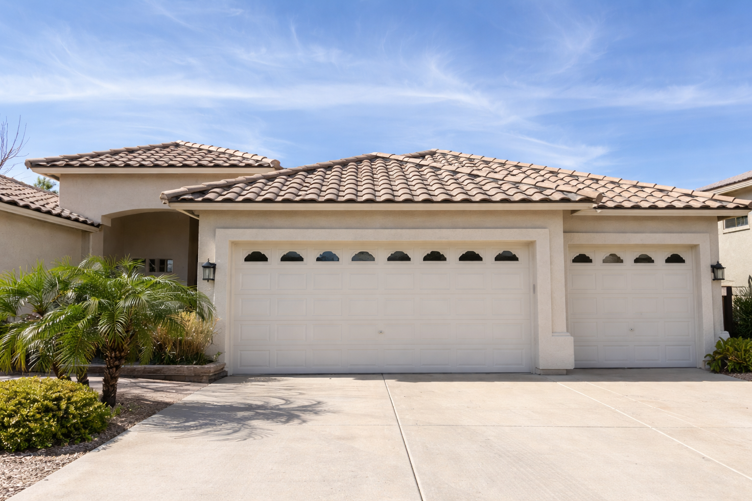 Exterior of a stucco house with a tile roof, an arched entry, palm trees, and two large garage doors, common in Glendale and Phoenix, Arizona.